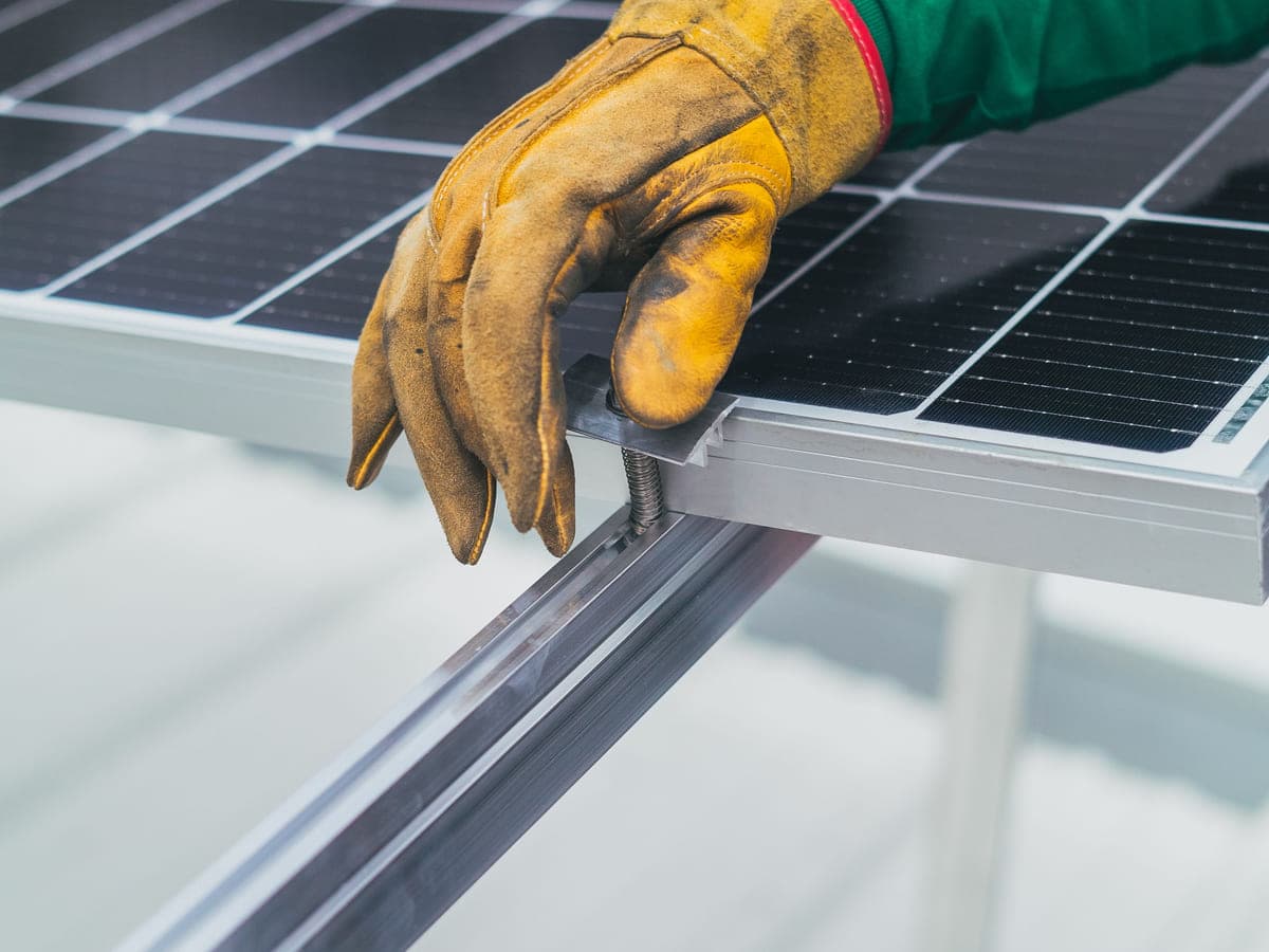 Gloved hand clamping a solar panel onto its mounting rail
